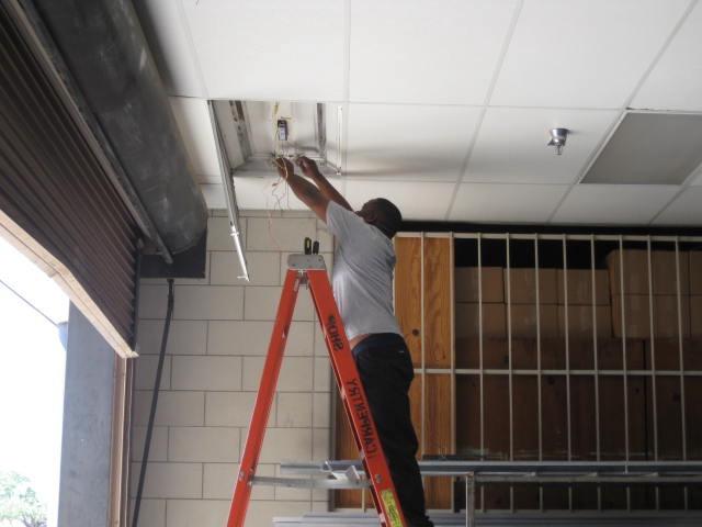 A Person fixing the wires on sealing using a lader